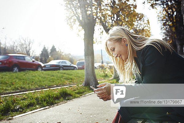 Lächelnde blonde Frau benutzt Smartphone im Freien