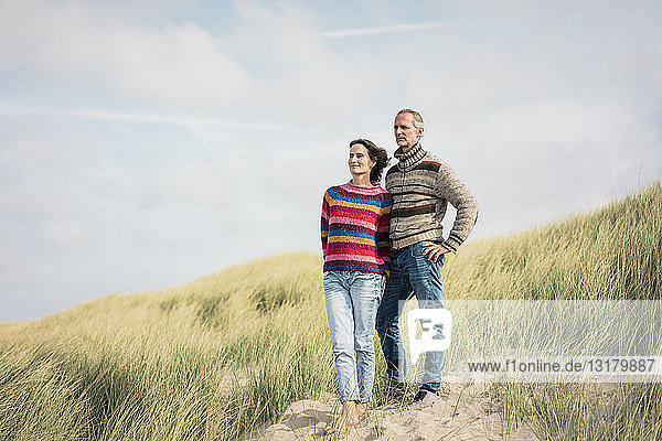 Mature couple standing in the dunes  with arms around