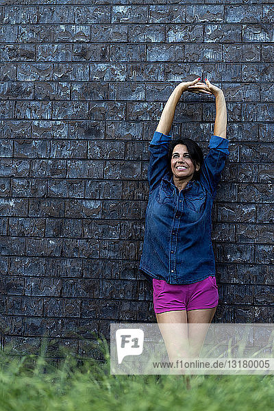 Smiling woman standing at brick wall stretching