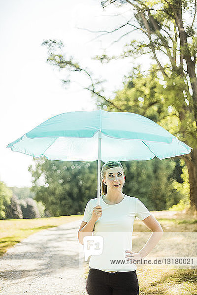 Sportliche junge Frau  die in einem Park steht und einen Sonnenschirm hält