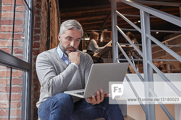 Businessman sitting on stairs of modern office  using laptop