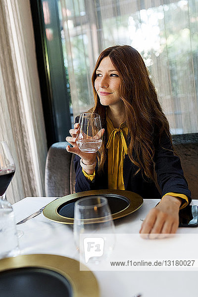 Lächelnde Frau sitzt am Tisch in einem Restaurant und trinkt ein Glas Wasser