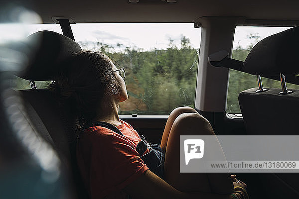 Junge Frau sitzt auf der Rückbank eines Lieferwagens  schaut aus dem Fenster und reist durch Norwegen