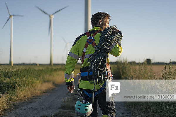 Techniker  der mit Kletterausrüstung einen Feldweg an einem Windpark begeht