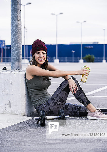 Young woman sitting on ground after dumbbell training  drinking juice