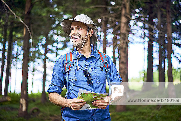 Smiling man holding a map hiking in the forest