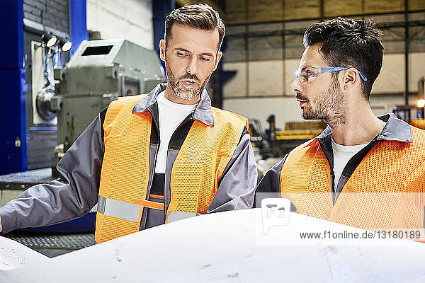 Zwei Männer in Arbeitsschutzkleidung besprechen Plan in der Fabrik