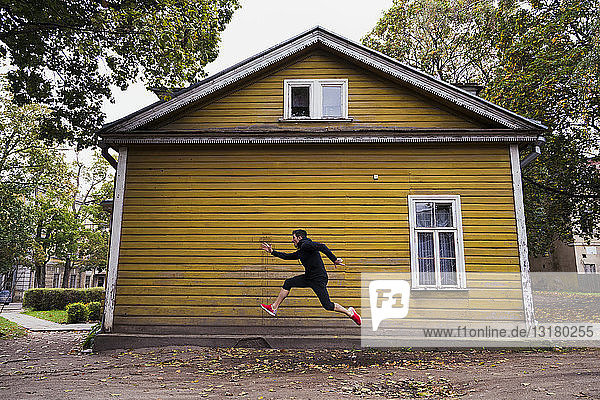 Dynamischer Athlet springt vor einem gelben Holzhaus