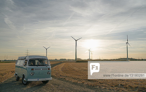 Couple in camper van in rural landscape with wind turbines at sunset