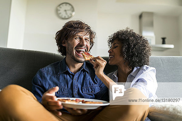 Happy couple sitting on couch eating pizza