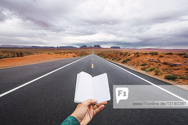 USA  Utah  Hand hält leeres Notizbuch über die Straße zum Monument Valley