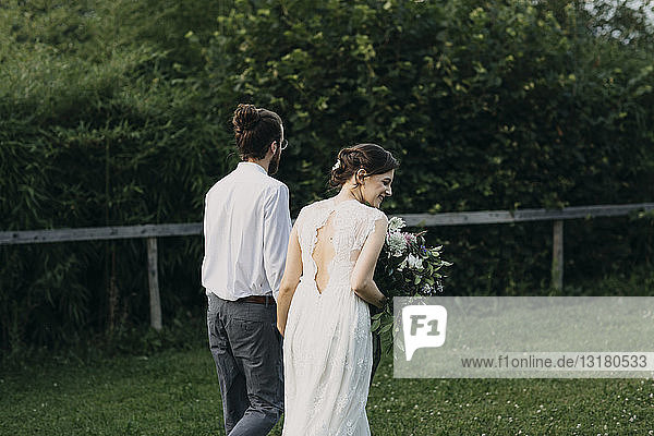 Rückansicht von Braut und Bräutigam beim Spaziergang auf der Wiese