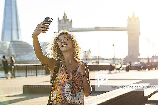 UK  London  lächelnde junge Frau beim Selfie mit der Tower Bridge im Hintergrund