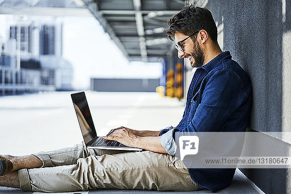 Smiling young man sitting on the ground using laptop