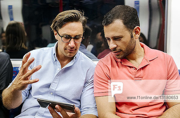 Porträt von zwei Freunden  die sich ein Handy in der U-Bahn teilen
