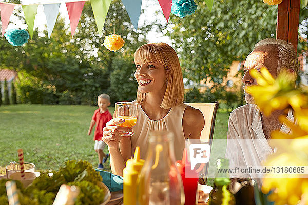 Lächelnde Frau trinkt Orangensaft auf einer Gartenparty