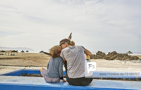 Chile  Arica  Mutter sitzt mit ihrem Sohn an einer Mauer am Strand