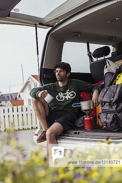Junger Mann sitzt im Wohnwagen und bereitet Kaffee auf einem Campingkocher zu