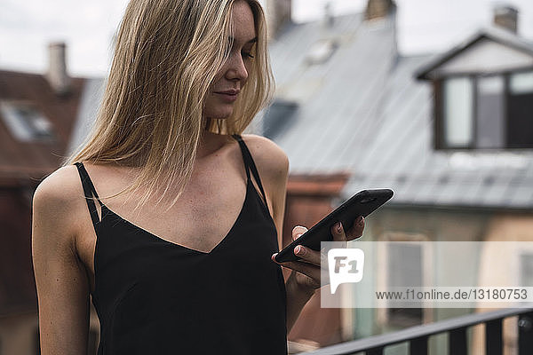 Blonde Frau auf dem Balkon mit Blick auf Handy