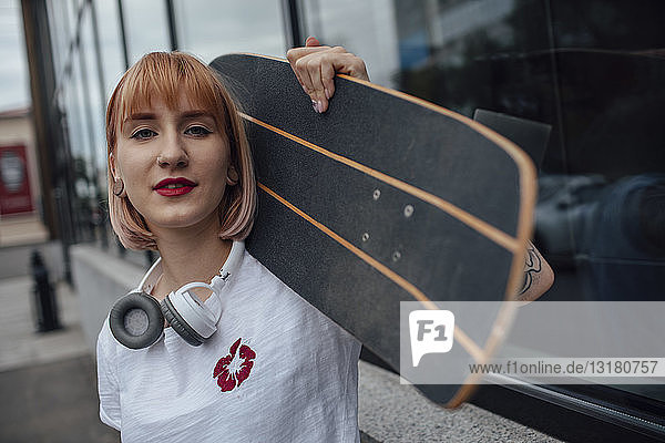 Porträt einer selbstbewussten jungen Frau  die ein Carver-Skateboard vor einem Gebäude hält