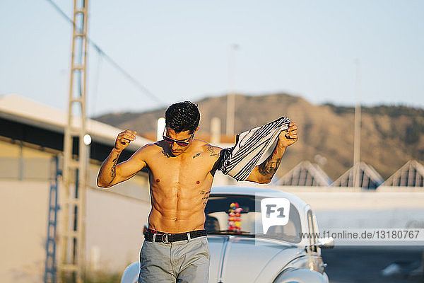 Man walking shirtless in front of a vintage car