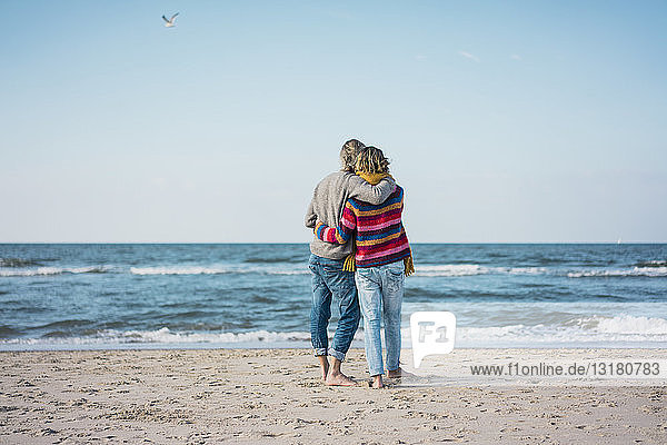 ture couple standing on the beach with arms around  looking at the sea