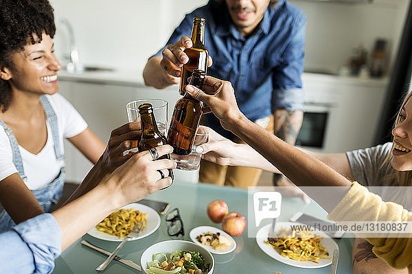 Fröhliche Freunde klirren mit Bierflaschen am Esstisch