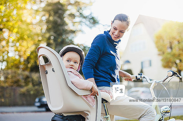 Mutter und Tochter fahren Fahrrad,  das Baby trägt einen Helm und sitzt im Kindersitz