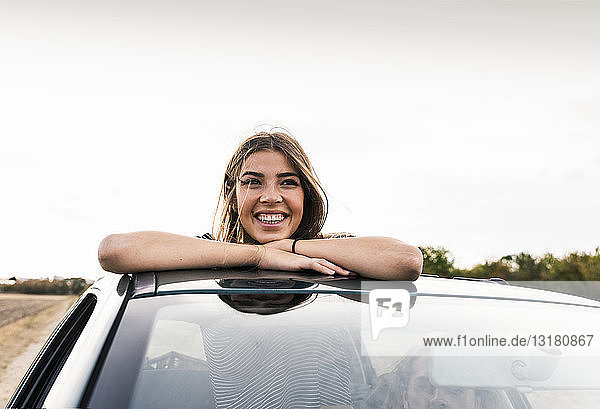 Lächelnde junge Frau schaut aus dem Schiebedach eines Autos