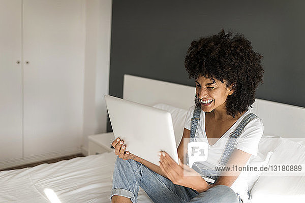Glückliche Frau sitzt auf dem Bett und schaut auf die Tablette