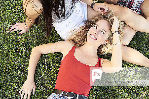 Porträt einer jungen Frau  die mit Freunden im Gras liegt und Musik hört