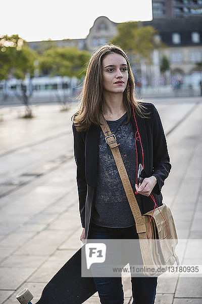 Young woman with longboard and cell phone in the city on the move