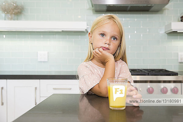 Porträt eines nachdenklichen Mädchens in der Küche mit einem Glas Orangensaft