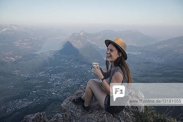 Schweiz  Grosse Mythen  glückliche junge Frau auf einer Wanderung  die mit einer Tasse auf einem Felsen sitzt
