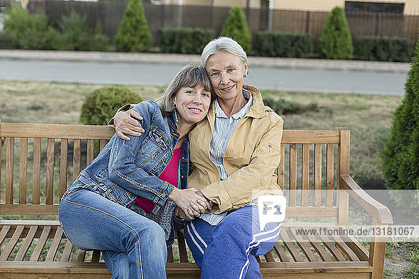 Porträt einer älteren Frau  die zusammen mit ihrer erwachsenen Tochter auf einer Bank sitzt