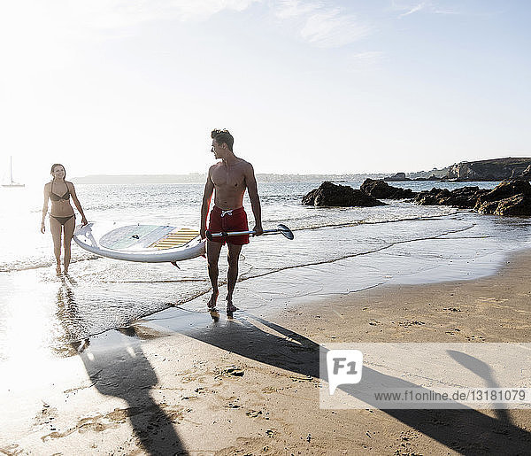 France  Brittany  young couple carrying an SUP board at the sea together