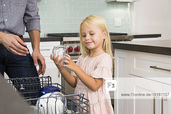 Mädchen hilft Vater beim Abräumen des Geschirrspülers in der Küche