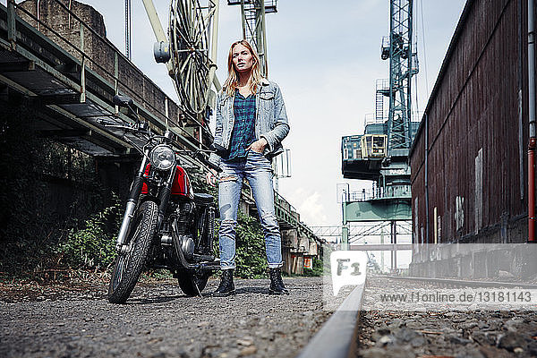 Porträt einer selbstbewussten jungen Frau  die neben einem Motorrad steht