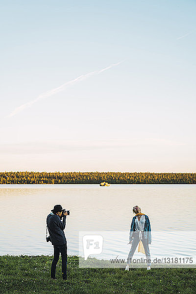 Junger Mann fotografiert junge Frau an einem See