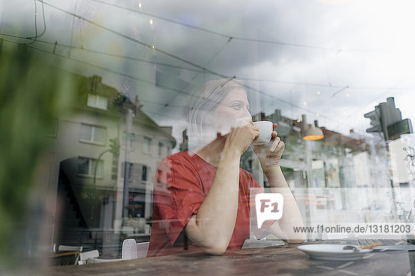 Junge Frau mit einer Tasse Kaffee hinter einer Fensterscheibe in einem Cafe