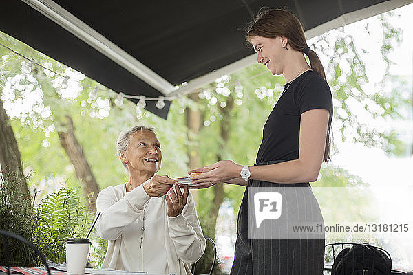 Kellnerin überreicht lächelnden älteren Frauen in einem Café im Freien einen Teller