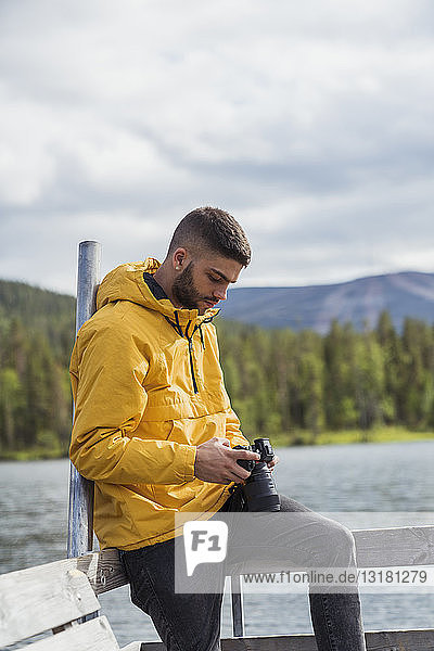 Finnland  Lappland  junger Mann mit einer Kamera auf einem Steg an einem See