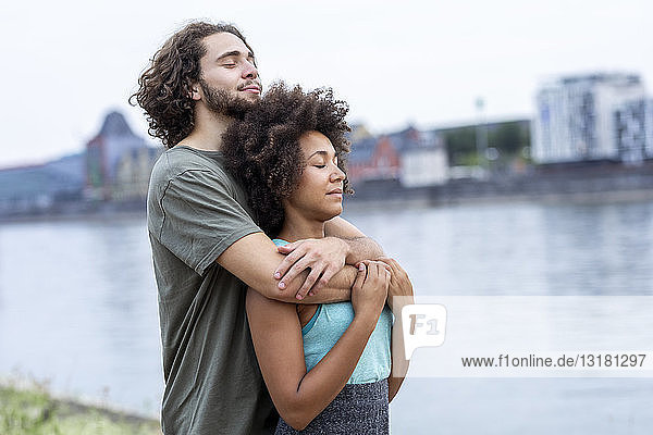 Deutschland  Köln  junges Paar umarmt sich am Flussufer