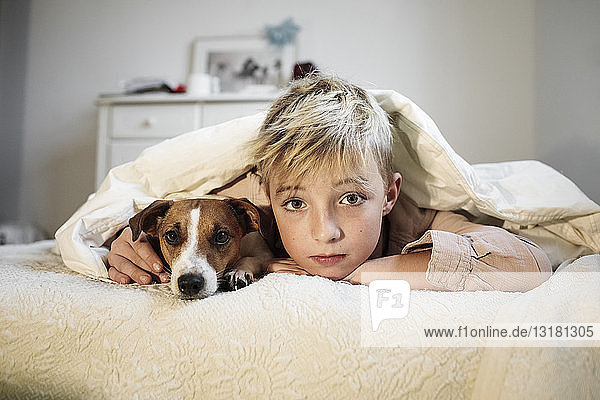 Portrait of blond boy and his Jack Russel Terrier lying together on bed
