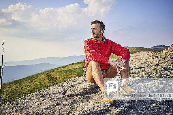 Mann sitzt auf Fels und genießt ruhige Momente beim Wandern