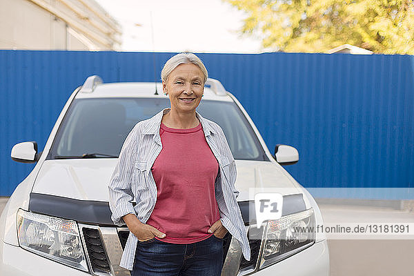 Porträt einer lächelnden älteren Frau  die vor ihrem Auto steht