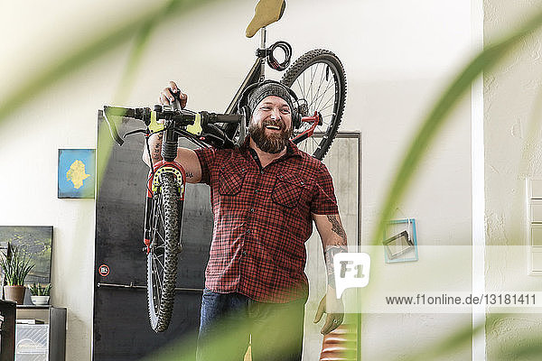 Lachender Mann mit Kopfhörern trägt Fahrrad im Büro