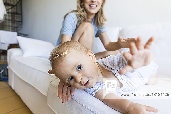 Porträt eines kleinen Mädchens  das auf einer Couch liegt und von seiner Mutter beobachtet wird