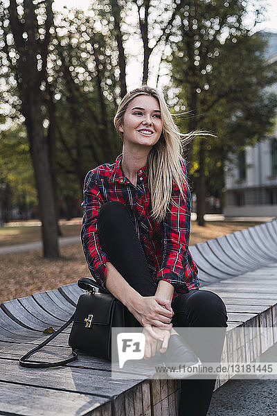 Porträt einer modischen jungen Frau mit Handtasche auf einer Bank im Freien sitzend