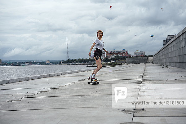 Junge Frau fährt Carver-Skateboard am Flussufer